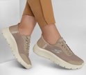 Voeten in taupe Skechers GO WALK sneakers met mesh bovenwerk, zilveren S-logo en witte zolen.