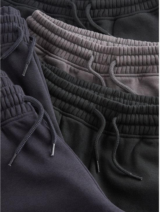 Close-up van de taillebanden met trekkoorden van meerdere donkere joggingbroeken.