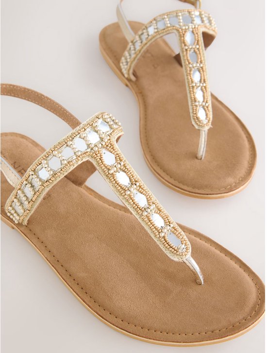 Twee gouden sandalen met platte zool, versierd met parels en spiegeltjes op de bandjes en teenstuk.