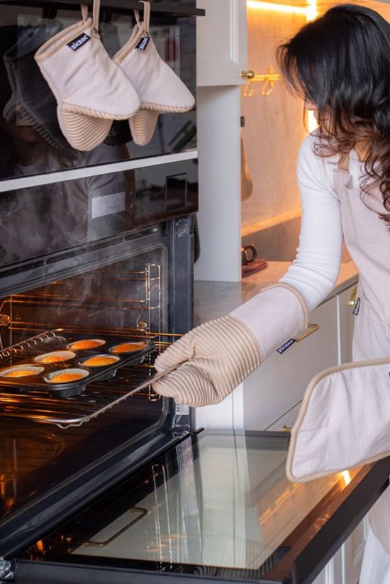 Vrouw in schort gebruikt beige ovenwant om bakplaat uit oven te halen.