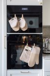 Twee beige ovenwanten en een pannenlap hangen aan een oven.