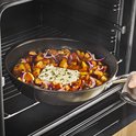 Man plaatst een pan met geroosterde groenten en kaas in een oven.