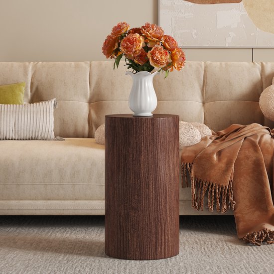 Ronde walnoothouten bijzettafel naast een beige bank met oranje plaid, met een vaas met oranje bloemen.
