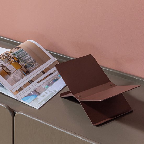 Een open boek met interieurfoto's ligt naast een bruine metalen boekenstandaard.