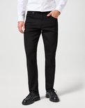 Model draagt zwarte jeans en een wit overhemd, staand.