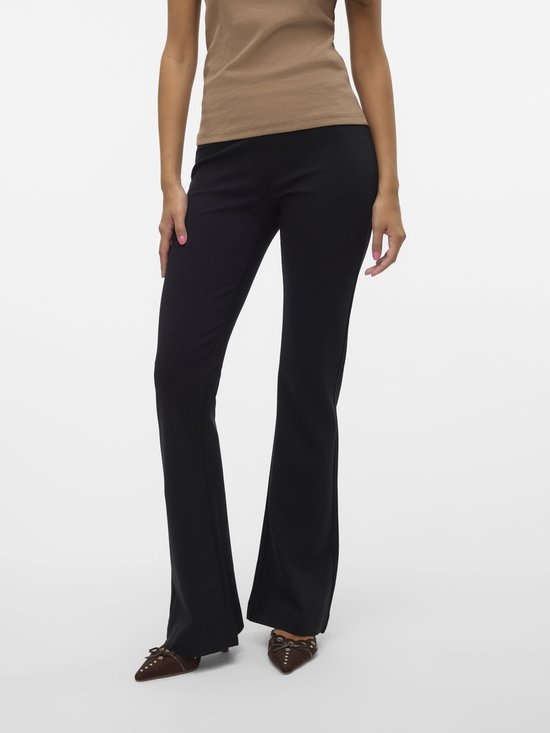 Vrouw in beige top en zwarte flared broek, schoenen zichtbaar.