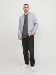 Man draagt een lichtgrijze hoodie met rits, donkergrijs T-shirt en zwarte jeans met scheuren.