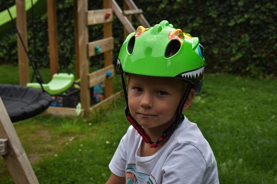 Groene dinosaurus kinderhelm met grote blauwe ogen en witte tanden. Gedragen door een jongen.