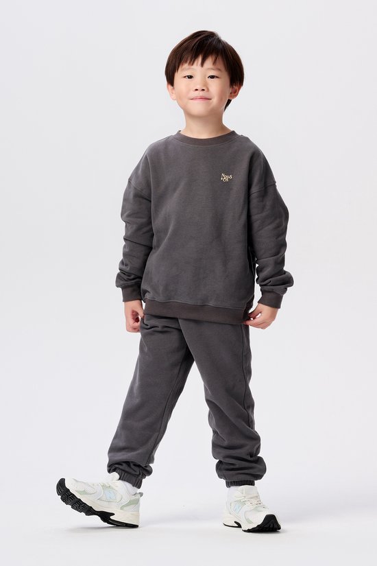 Jongetje in donkergrijs joggingpak met ronde hals en witte sneakers.