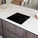 Zwarte inductiebeschermer met marmerprint met gouden details, op een wit composiet aanrecht.