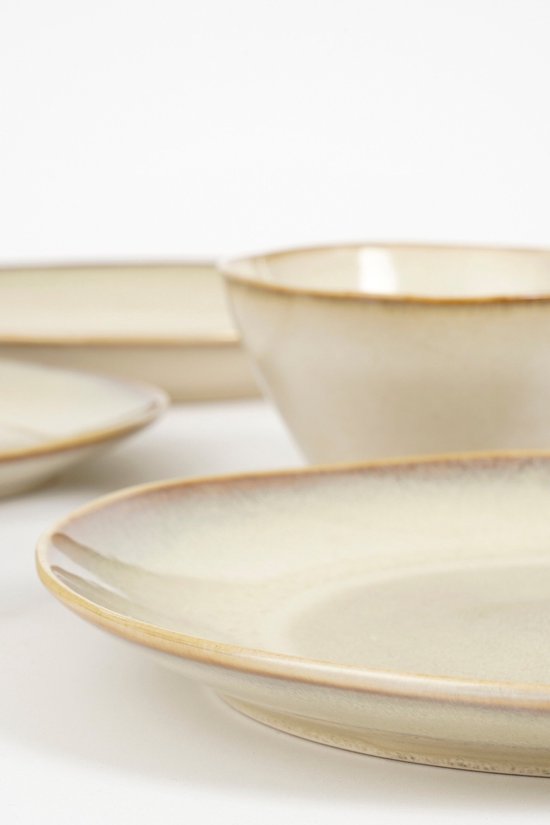 Verschillende beige borden en een kom met een bruine rand op een witte achtergrond, de focus ligt op de voorste borden.