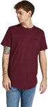 Man met tatoeages op zijn arm draagt een bordeauxrode t-shirt met korte mouwen en ronde hals, met een klein logo op de borst, staand.