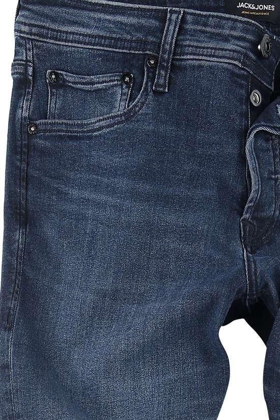 Detail van de tailleband van een donkerblauwe jeans, met zakken en knopen.