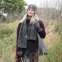 Model in grijze gebreide sjaal, muts en handschoenen. Draagt een bordeauxrode vest en zwarte jurk.