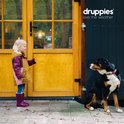 Meisje met paarse laarzen wijst naar een hond die naast een gele deur zit.