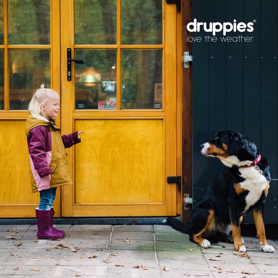 Meisje met paarse laarzen wijst naar een hond die naast een gele deur zit.