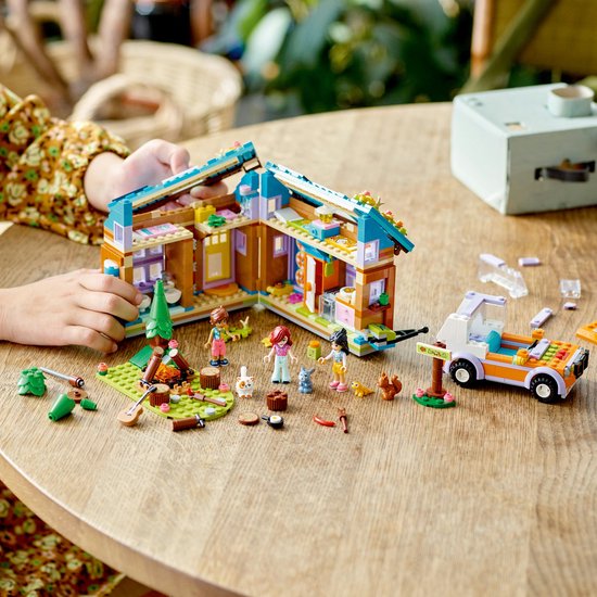 Een kind bouwt een LEGO Friends huisje met camper, kampvuur, bomen en dieren.
