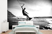 Behang - Fotobehang Een man aan het wakeboarden op rustig zeewater - zwart wit - Breedte 420 cm x hoogte 280 cm