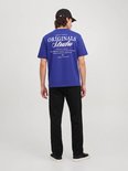Achteraanzicht van model in blauw T-shirt met grote witte 'ORIGINALS Studio' tekst op de rug en zwarte broek.