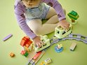 Een jong kind met een paarse trui en spijkerbroek speelt met een lichtgroene trein en rails.
