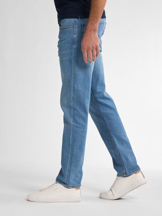 Zijaanzicht van een model in lichtblauwe Petrol Industries jeans en witte sneakers.
