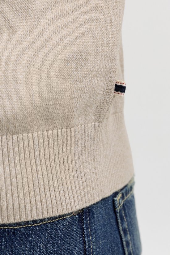 Detail van de onderkant van een beige gebreide trui met label.