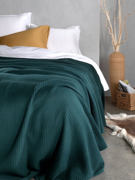 Donkergroene wafelstructuur bedsprei over een bed met witte en okergele kussens.