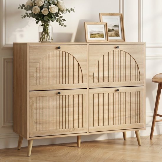 Licht houten schoenenkast met vier kleppen, elk met gebogen ribbelpatroon en een zwart handvat. Twee fotolijsten en een vaas met bloemen staan bovenop.