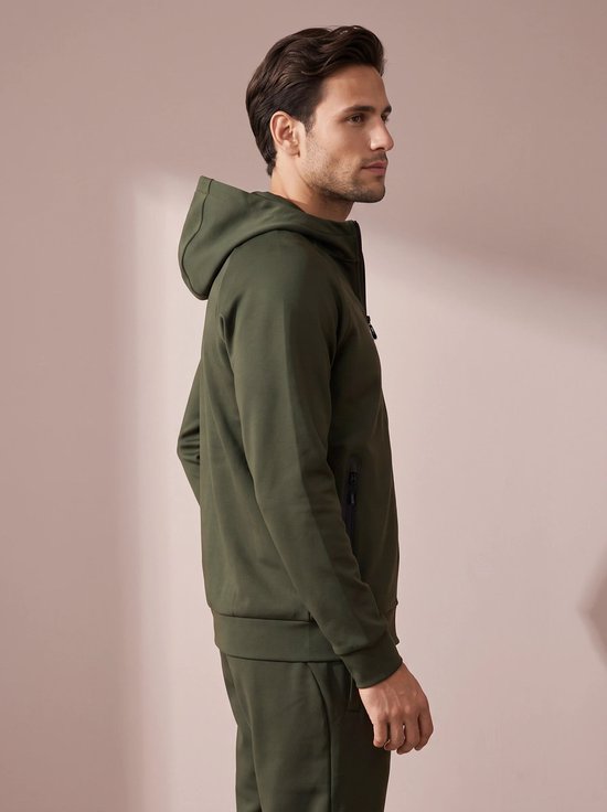 Man zijdelings gezien, draagt een olijfgroene hoodie met capuchon en ritszakken.
