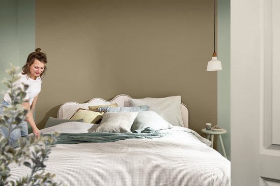 Slaapkamer met een vrouw die het bed opmaakt. Muur geschilderd in de kleur Earthly Calm.