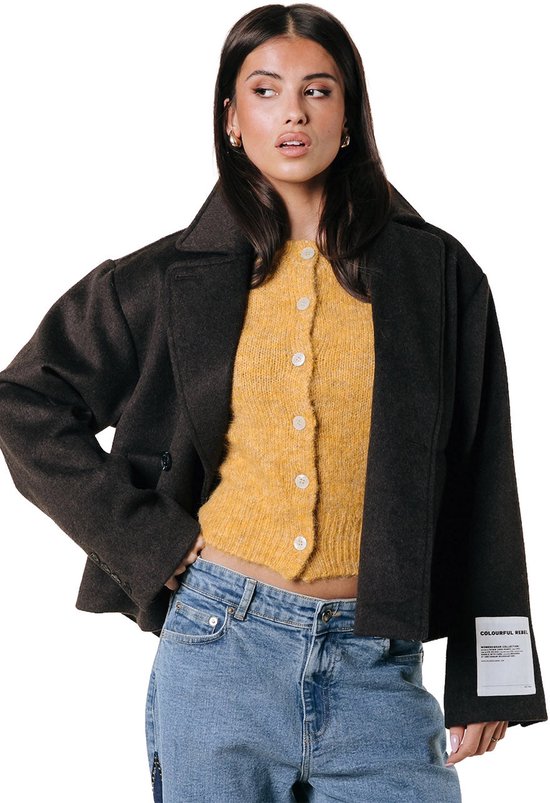 Een vrouw draagt een donkerbruine korte wollen jas over een geel vestje en blauwe jeans. Op de mouw zit een label met 'COLOURFUL REBEL'.