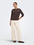 Vrouwenmodel met een donkerbruine trui met lange mouwen en een wit hartje op de borst. Gepaard met een crème broek.