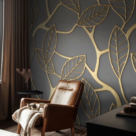 Un fauteuil en cuir marron avec un chat dessus, devant un mur à motif de feuilles dorées.