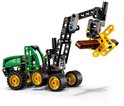 Groene en zwarte LEGO Technic John Deere 1470H houtoogstmachine met gele grijper die een bruine stam vasthoudt.