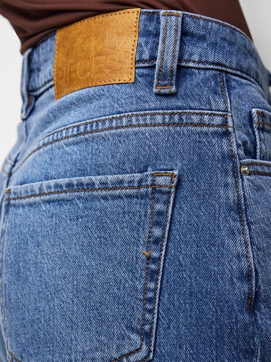 Close-up van de achterkant van de blauwe jeans met een bruin leren label met het logo 'PIECES' op de tailleband.