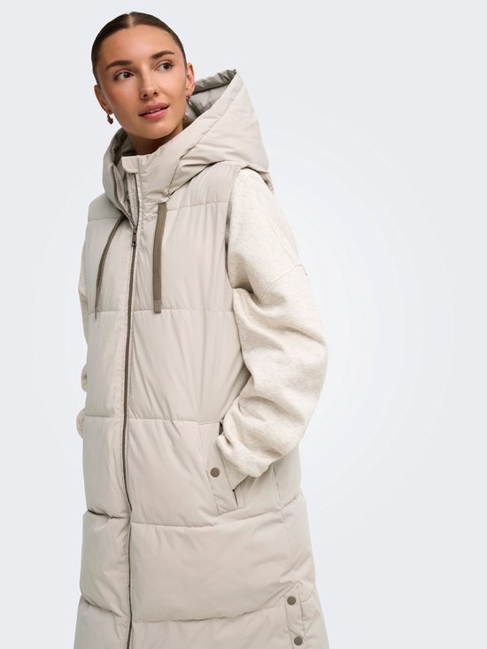Zijzicht van een model met een lange beige bodywarmer met capuchon, de rits is half geopend.