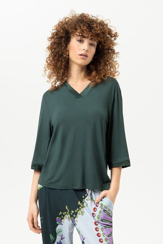 Model draagt een donkergroen Mey T-shirt met V-hals en driekwartmouwen, gecombineerd met een bedrukte broek.