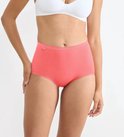 Model draagt een koraalkleurige maxi-slip met hoge taille en Sloggi-label.
