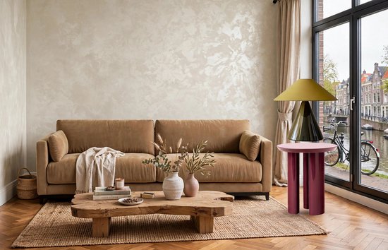 Een zandbruine bank in een woonkamer met een houten salontafel, een grote spiegelwand, en een raam met uitzicht op een gracht.