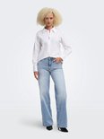 Model met blond krullend haar draagt een witte blouse en lichtblauwe ONLMADISON jeans met wijde pijpen.