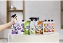 Hand houdt een Marcel's Green Soap sprayflacon vast voor een assortiment navulverpakkingen en flessen op een voetstuk.