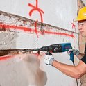 Vakman in gele helm hakt een bakstenen muur open met een blauwe Bosch Professional boorhamer.