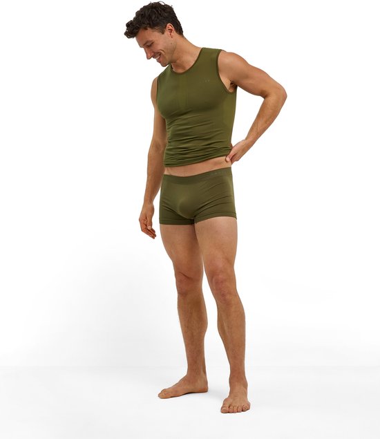 Man in een olijfgroen naadloos hemd en bijpassende boxershort van Falke, staand en glimlachend.