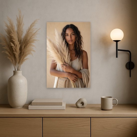 Canvas schilderij van een vrouw met pampasgras, hangend boven een houten dressoir met een vaas en lamp.