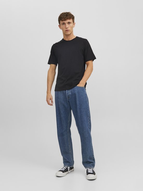 Man in een zwart T-shirt en spijkerbroek, handen in de zakken.