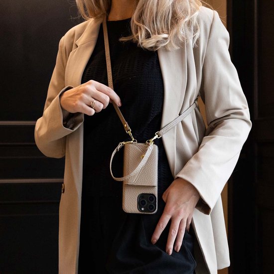 Een vrouw met een beige blazer draagt een taupe telefoonhoesje met koord en kaarthouder om haar nek.