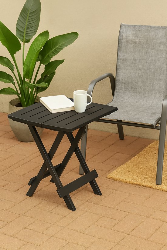 Zwarte inklapbare tafel naast een grote plant en een grijze stoel.