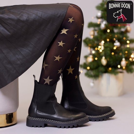 Zwarte panty met gouden glittersterren gedragen onder een zwarte rok en zwarte laarsjes.