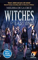 Vier vrouwen in elegante, duistere kleding staan voor brandende bomen. Titel: Witches of East End.