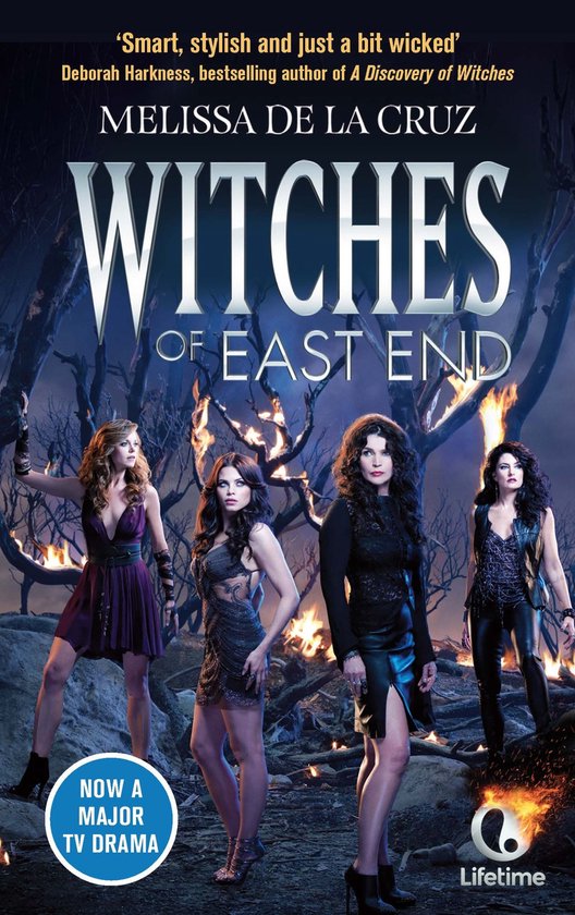 Vier vrouwen in elegante, duistere kleding staan voor brandende bomen. Titel: Witches of East End.
